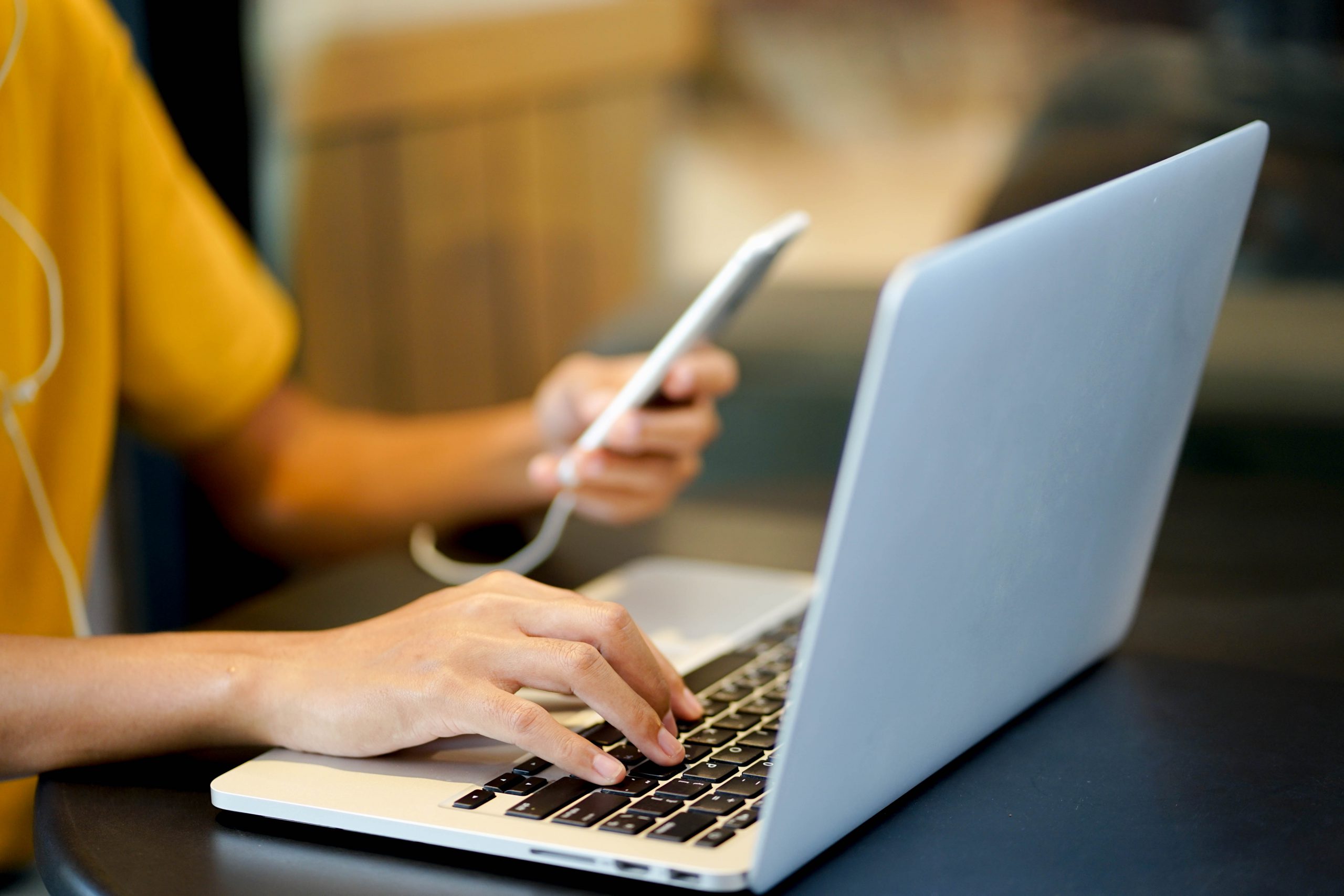 close up young girl hand typing o keyboard laptop while playing smartphone at coffee cafe shop , life style concept